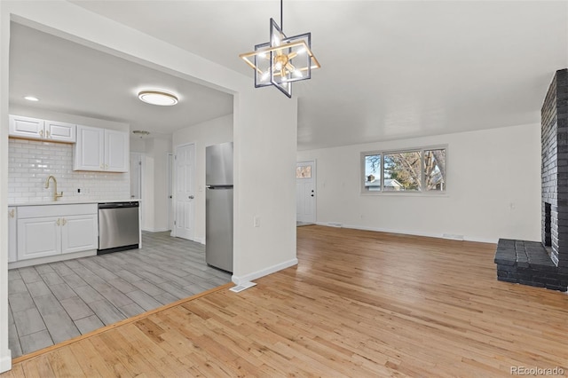 kitchen with white cabinetry, stainless steel appliances, decorative light fixtures, decorative backsplash, and a fireplace