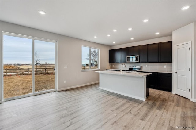 14441 Clover Dr, Mead, CO 80504 - kitchen with stainless steel microwave, a kitchen island with sink, light wood-style flooring, decorative backsplash, and light countertops
