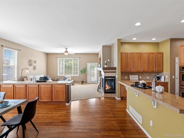 3853 S Malta St, Aurora, CO 80013 - kitchen with open floor plan, dark wood-type flooring, a tiled fireplace, ceiling fan, and recessed lighting