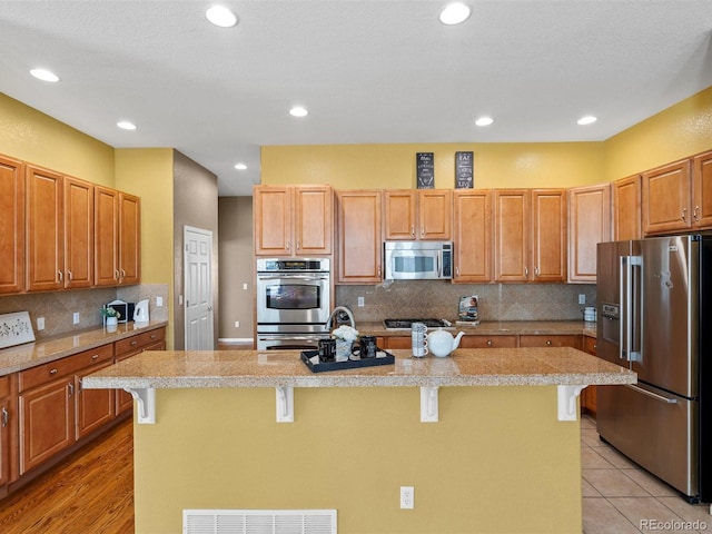 3853 S Malta St, Aurora, CO 80013 - kitchen with stainless steel appliances, a breakfast bar, a center island with sink, tasteful backsplash, and recessed lighting