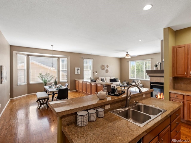 3853 S Malta St, Aurora, CO 80013 - kitchen with a sink, brown cabinets, light wood-type flooring, a tile fireplace, and baseboards