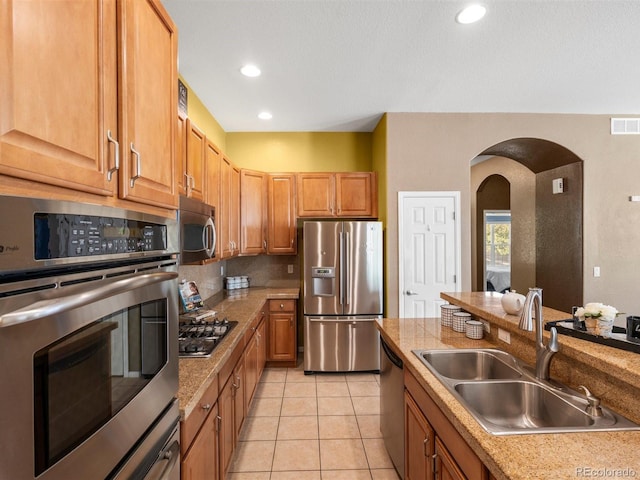 3853 S Malta St, Aurora, CO 80013 - kitchen featuring appliances with stainless steel finishes, a sink, arched walkways, decorative backsplash, and light tile patterned floors