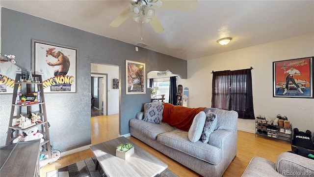 living room with visible vents, a ceiling fan, wood finished floors, baseboards, and a textured wall