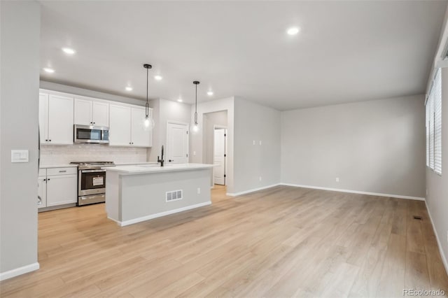 kitchen with white cabinetry, stainless steel appliances, backsplash, an island with sink, and decorative light fixtures