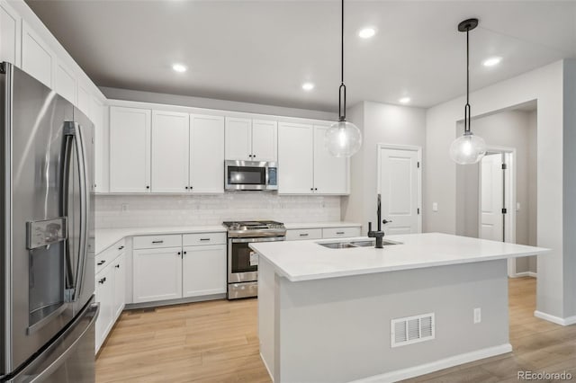 kitchen with a kitchen island with sink, white cabinets, sink, hanging light fixtures, and stainless steel appliances