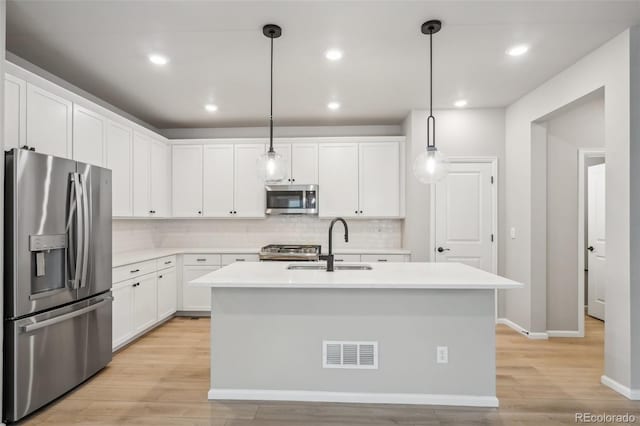 kitchen featuring sink, stainless steel appliances, pendant lighting, a center island with sink, and white cabinets