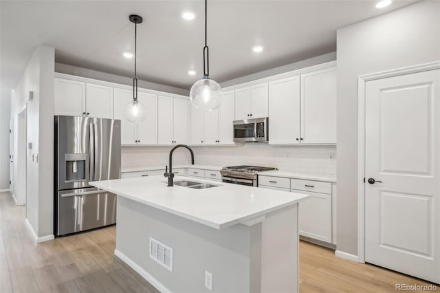 kitchen with appliances with stainless steel finishes, sink, white cabinets, hanging light fixtures, and an island with sink