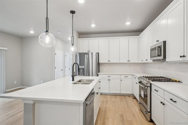 kitchen with sink, stainless steel appliances, pendant lighting, a kitchen island with sink, and white cabinets