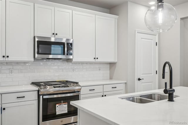 kitchen with appliances with stainless steel finishes, tasteful backsplash, sink, decorative light fixtures, and white cabinets