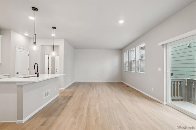 interior space featuring pendant lighting, light hardwood / wood-style floors, a center island with sink, and sink