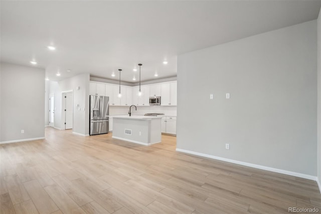 kitchen featuring sink, decorative light fixtures, a center island with sink, white cabinets, and appliances with stainless steel finishes