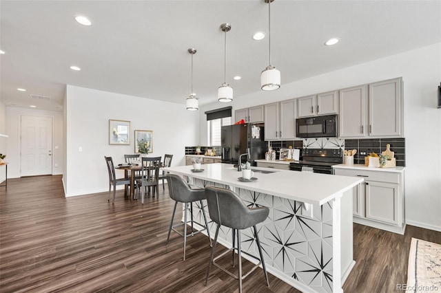 kitchen featuring black appliances, decorative light fixtures, an island with sink, dark wood-type flooring, and gray cabinetry