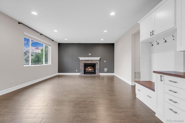 unfurnished living room with dark wood finished floors, baseboards, a stone fireplace, and recessed lighting