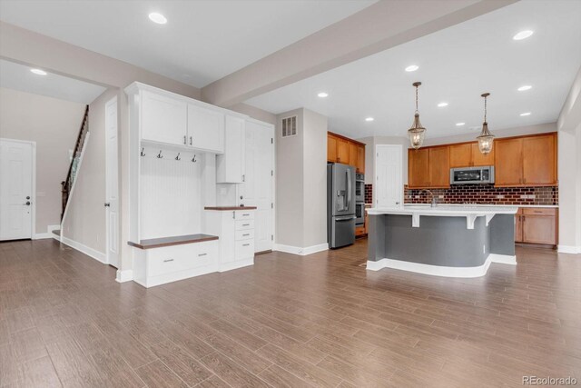 kitchen with stainless steel appliances, tasteful backsplash, a breakfast bar, baseboards, and a center island with sink