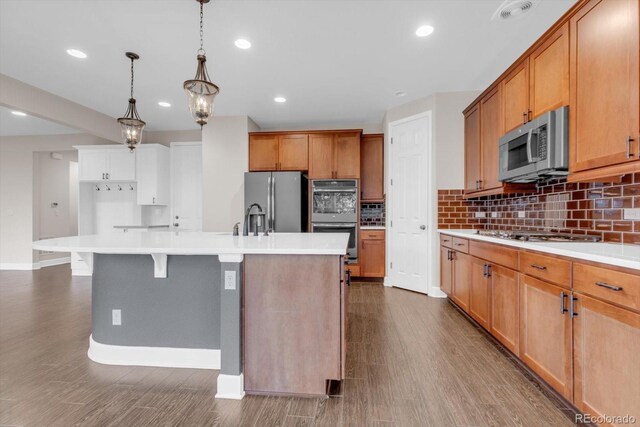 kitchen featuring appliances with stainless steel finishes, backsplash, dark wood-style floors, a kitchen island with sink, and baseboards
