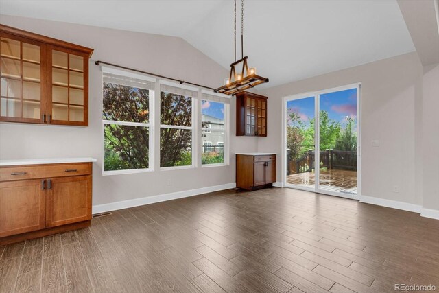 unfurnished dining area with a chandelier, dark wood-style flooring, baseboards, and lofted ceiling