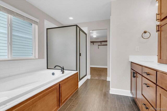 bathroom with a shower stall, a walk in closet, a bath, and vanity