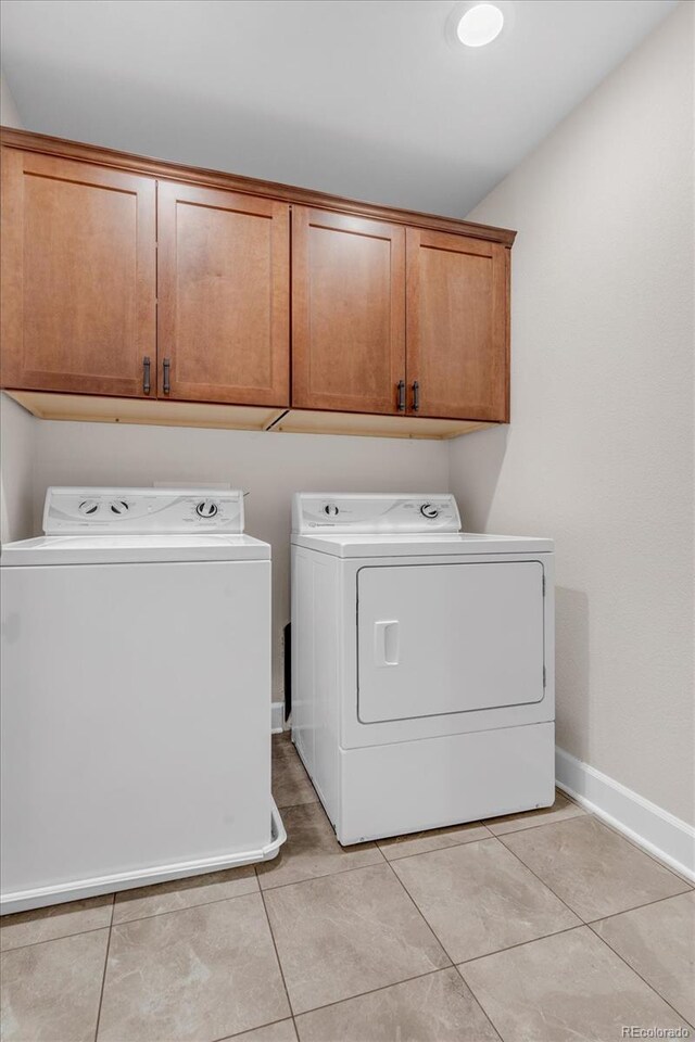 clothes washing area with separate washer and dryer, cabinet space, baseboards, and light tile patterned flooring