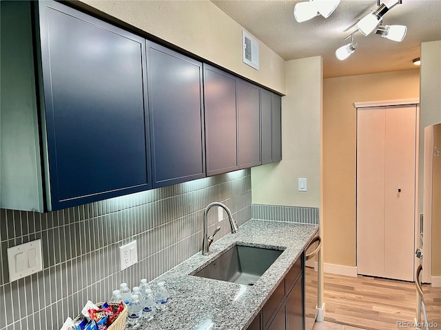 kitchen with sink, dishwasher, light stone counters, light hardwood / wood-style floors, and decorative backsplash