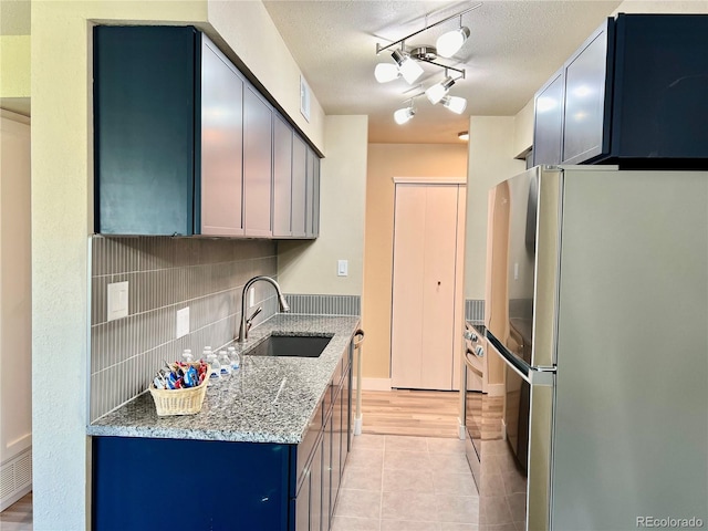 kitchen featuring stainless steel refrigerator, sink, backsplash, light stone countertops, and a textured ceiling