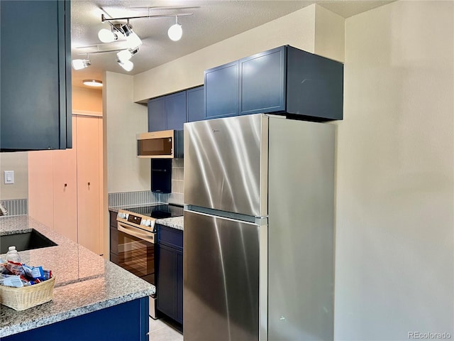 kitchen with light stone counters, appliances with stainless steel finishes, a textured ceiling, blue cabinetry, and sink