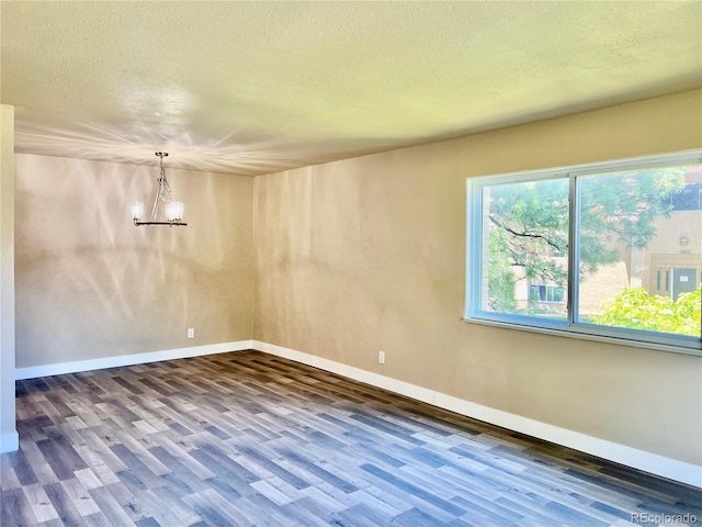 empty room featuring dark wood-type flooring, a textured ceiling, and a chandelier