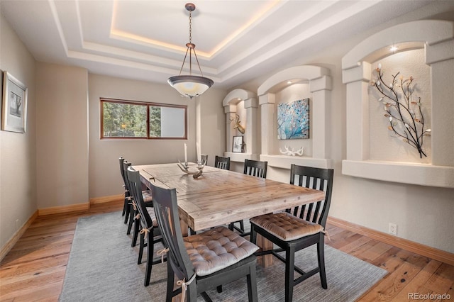 dining space with a raised ceiling, baseboards, and light wood-style flooring