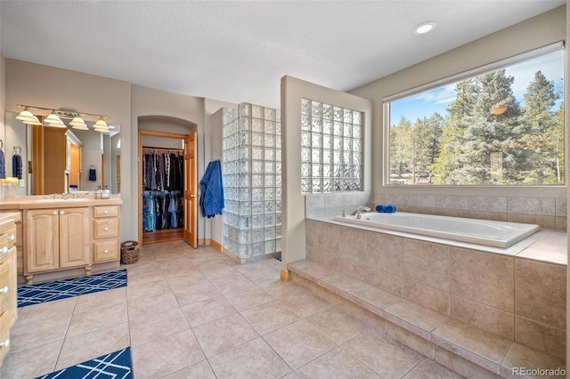 bathroom featuring vanity, tile patterned flooring, a textured ceiling, a walk in closet, and a bath