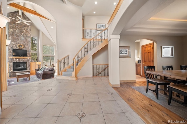 foyer entrance with a stone fireplace, a ceiling fan, stairs, beam ceiling, and arched walkways