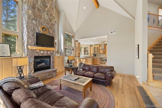 living area featuring visible vents, a fireplace, stairs, wood-type flooring, and high vaulted ceiling