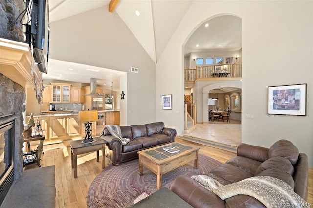living area with high vaulted ceiling, arched walkways, a fireplace, and visible vents