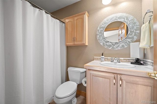 full bath with toilet, vanity, and a textured wall