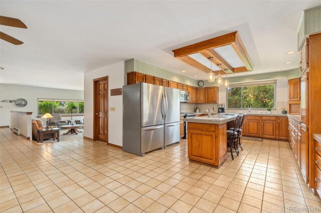 kitchen with a center island with sink, stainless steel appliances, light tile patterned floors, sink, and a breakfast bar