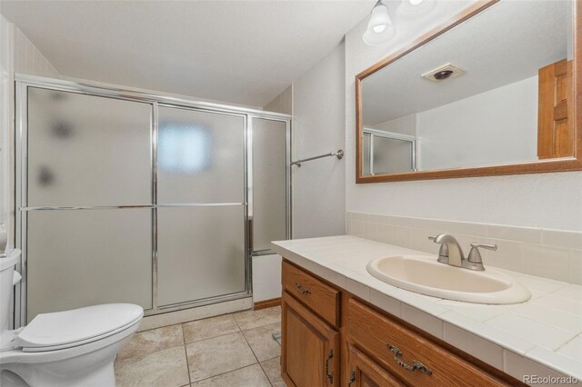 bathroom featuring toilet, tile patterned flooring, tasteful backsplash, an enclosed shower, and vanity