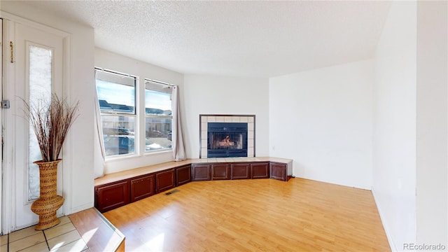 unfurnished living room featuring a textured ceiling, a tile fireplace, and light hardwood / wood-style flooring