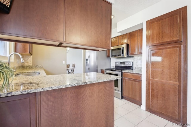 kitchen featuring light tile patterned floors, light stone counters, a peninsula, a sink, and appliances with stainless steel finishes