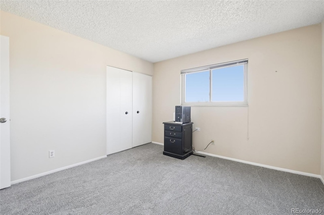 unfurnished bedroom featuring carpet, a closet, a textured ceiling, and baseboards