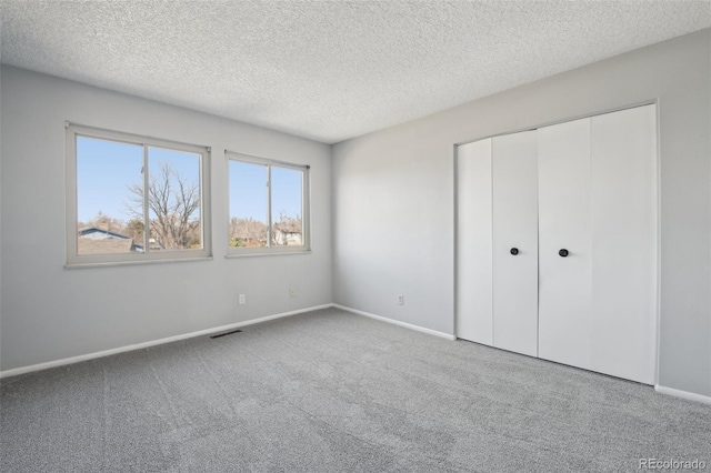 unfurnished bedroom with baseboards, visible vents, carpet, a textured ceiling, and a closet