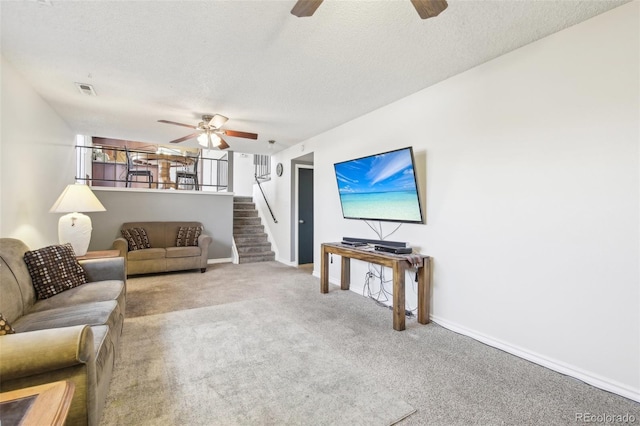 living area with a textured ceiling, carpet floors, a ceiling fan, baseboards, and stairs