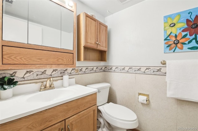 half bath featuring tile walls, visible vents, toilet, wainscoting, and vanity