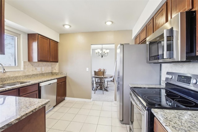 kitchen with stainless steel appliances, a sink, a chandelier, light stone countertops, and backsplash
