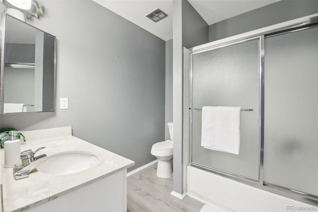 bathroom featuring wood finished floors, toilet, vanity, baseboards, and bath / shower combo with glass door