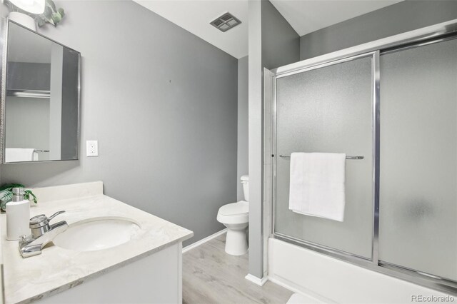 12097 E Mexico Ave, Aurora, CO 80012 - bathroom featuring wood finished floors, toilet, vanity, baseboards, and bath / shower combo with glass door
