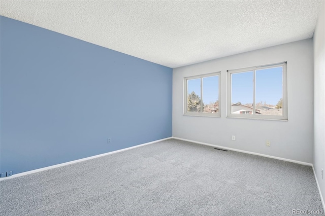 carpeted spare room featuring a textured ceiling and baseboards