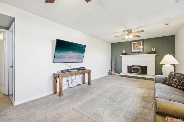 living room featuring a ceiling fan, carpet flooring, a fireplace with raised hearth, and a textured ceiling