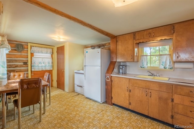 kitchen with freestanding refrigerator, brown cabinets, a sink, and light countertops