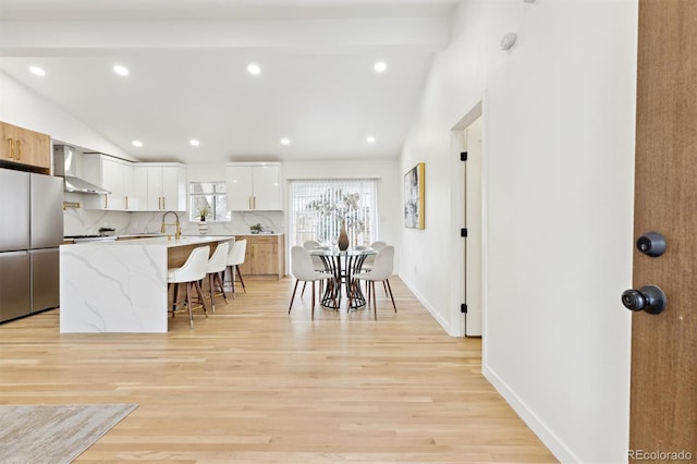 kitchen with wall chimney range hood, freestanding refrigerator, vaulted ceiling, a kitchen breakfast bar, and modern cabinets