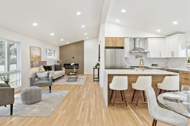 kitchen featuring light wood finished floors, lofted ceiling, freestanding refrigerator, a kitchen breakfast bar, and wall chimney range hood