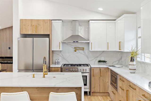 kitchen featuring backsplash, wall chimney range hood, lofted ceiling, appliances with stainless steel finishes, and modern cabinets