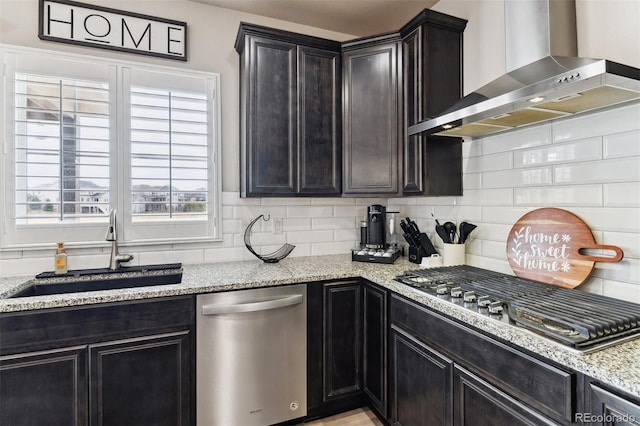 kitchen with stainless steel appliances, tasteful backsplash, a sink, light stone counters, and wall chimney range hood